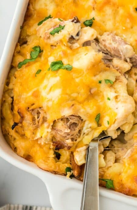 A spoon scooping a serving of the pulled pork mac and cheese off a casserole dish, showing the creamy macaroni and pulled pork filling