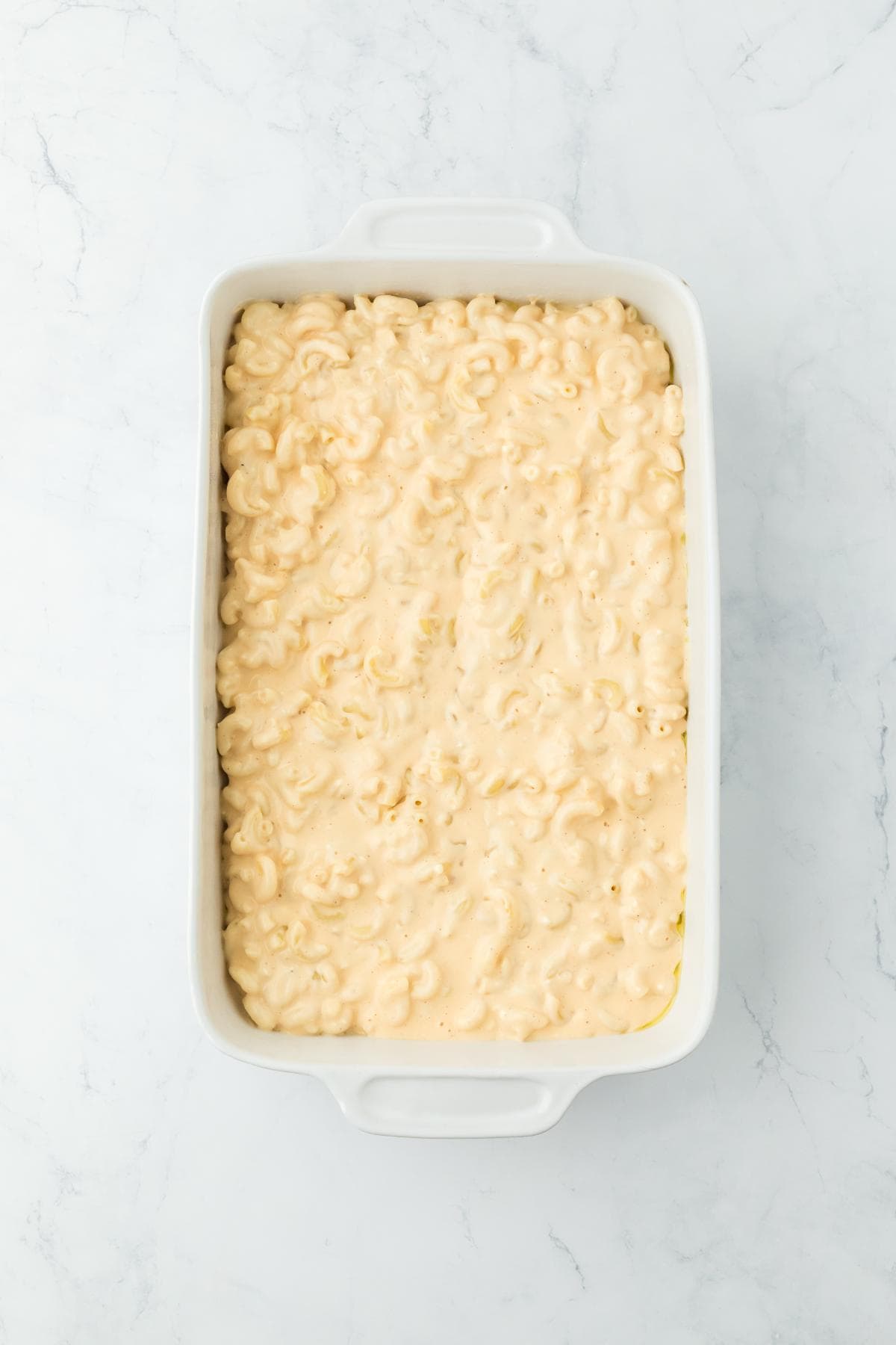 A baking dish filled with creamy macaroni and cheese, spread evenly for baking