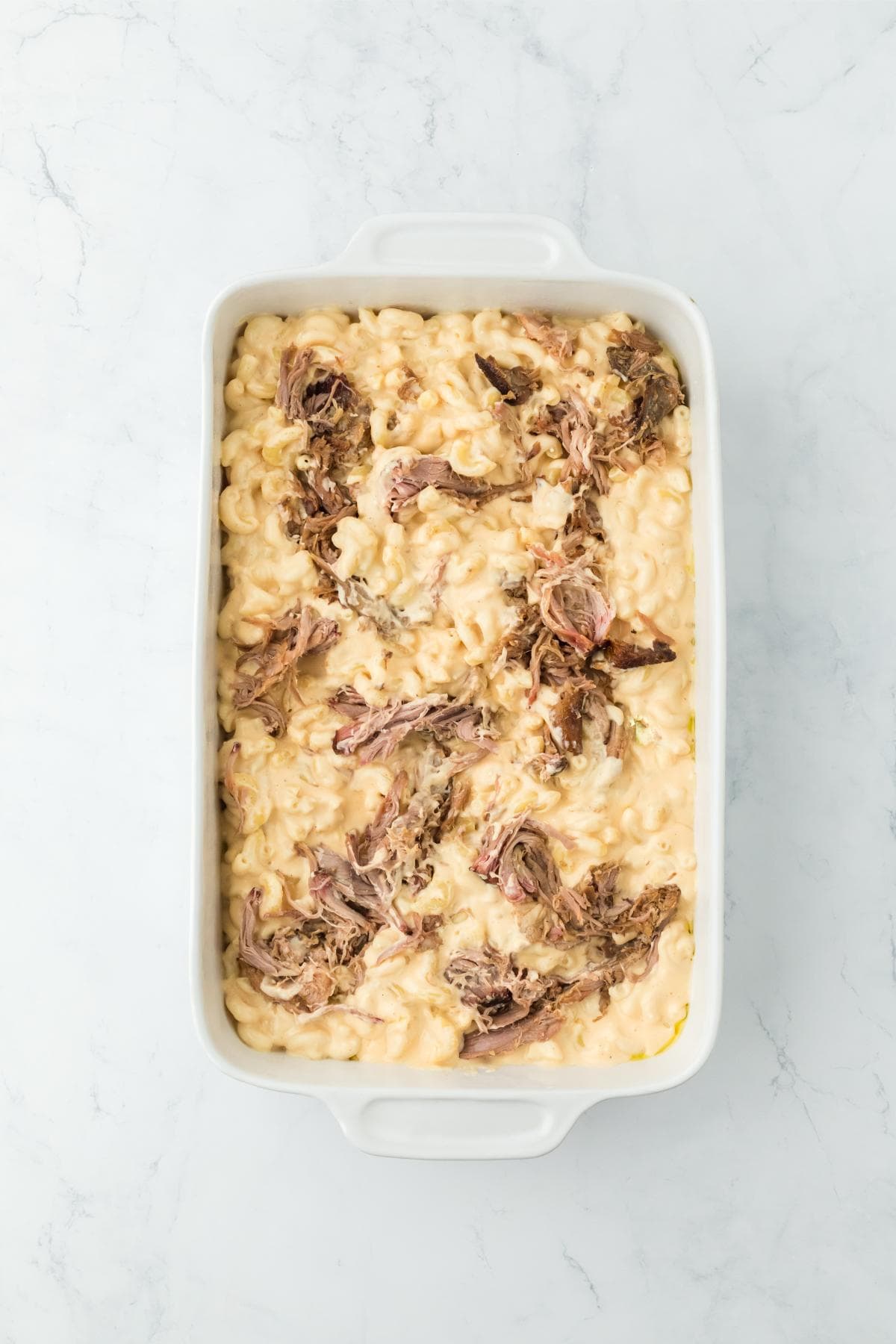 Mac and cheese in the casserole dish before baking, showing creamy pasta mixed with shredded pulled pork