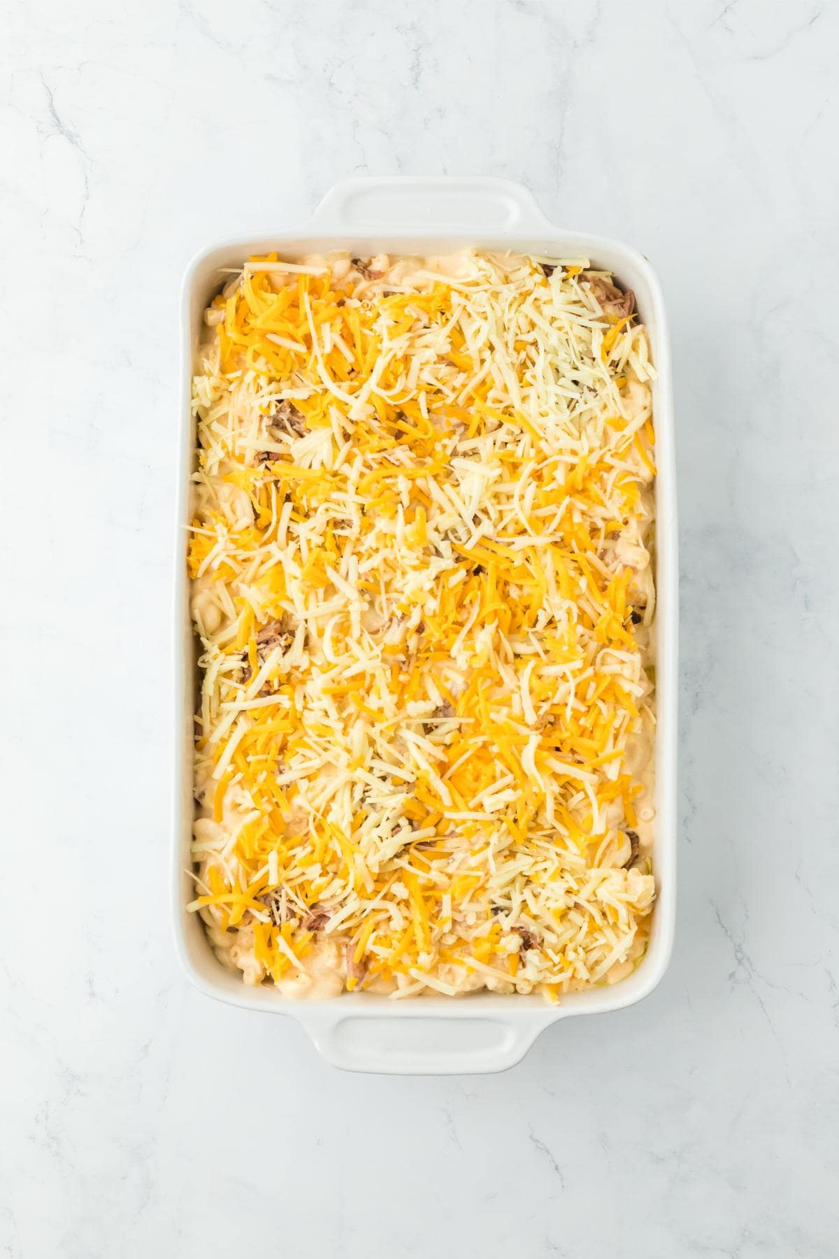 A view of the mac and cheese topped with shredded cheddar and mozzarella cheese, ready to be baked