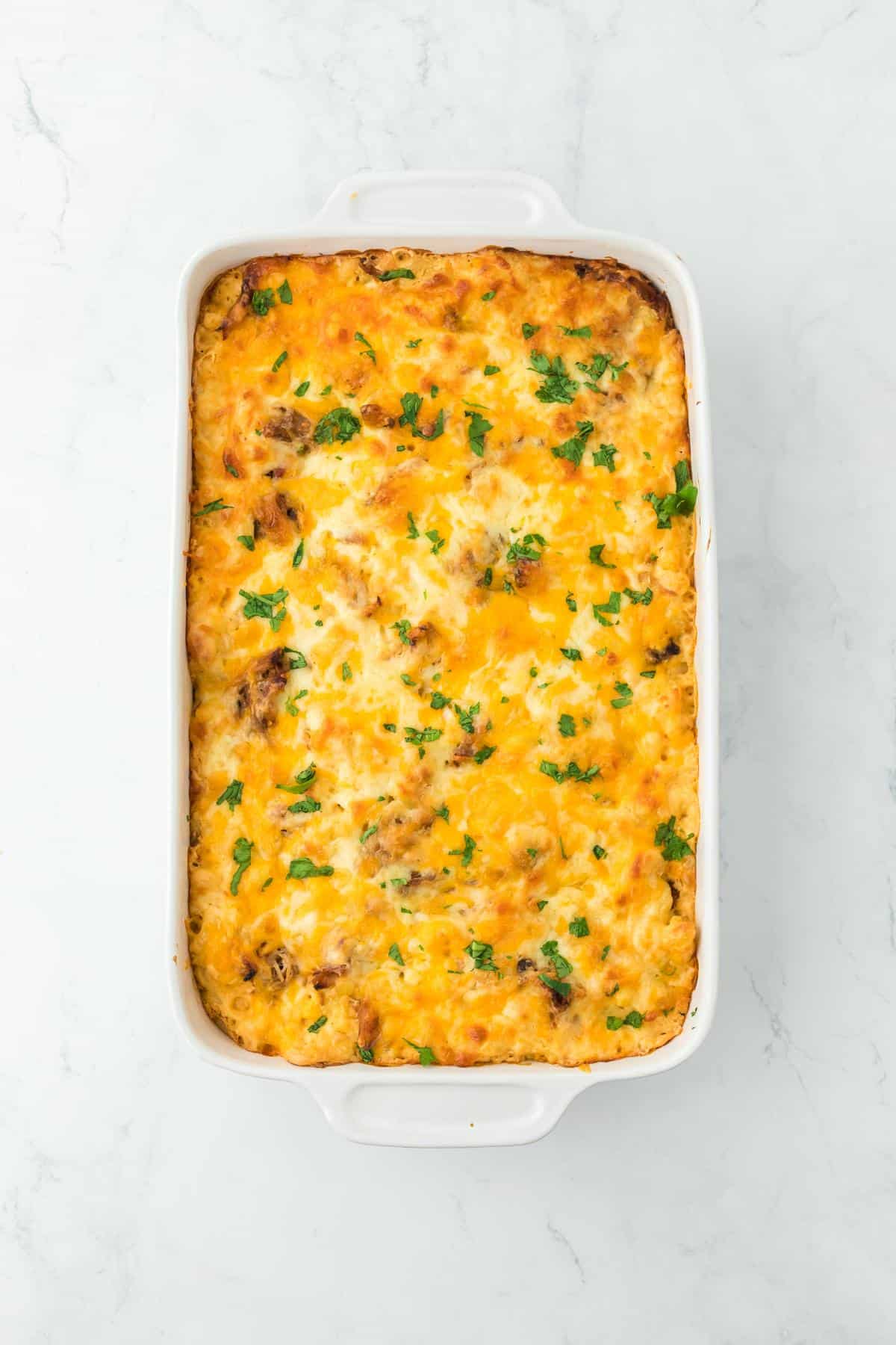 The fully baked pulled pork mac and cheese in a casserole dish, golden brown and garnished with parsley