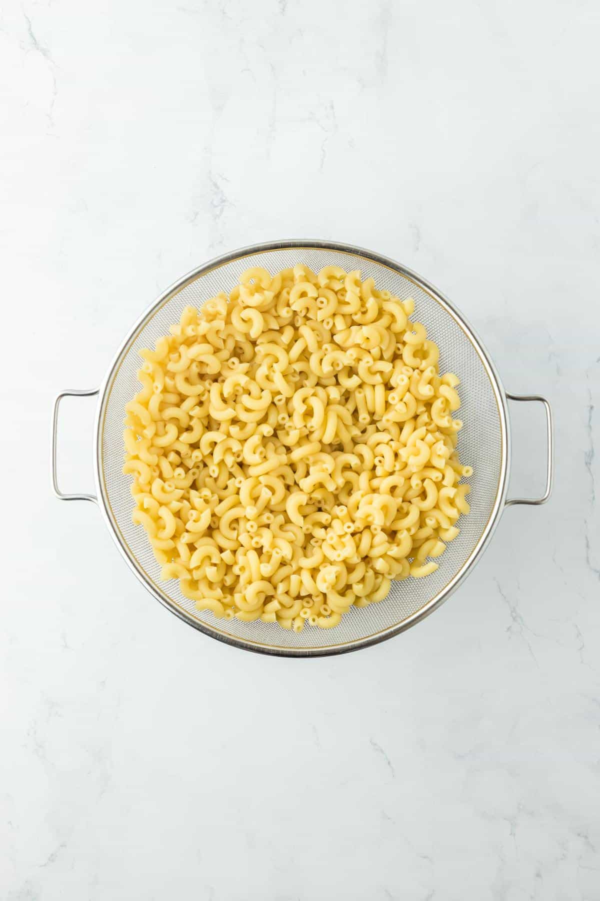 Cooked elbow macaroni being drained in a large colander