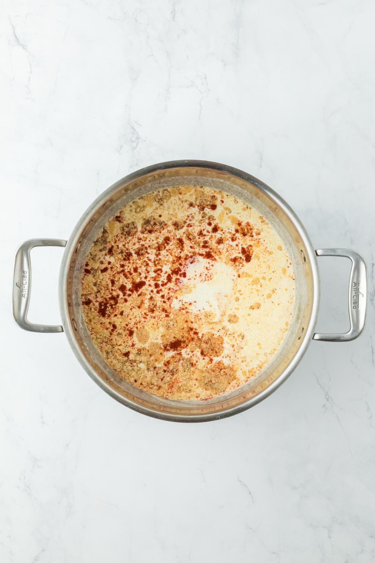 A pot with milk and spices added to the roux, ready to be mixed for a cheese sauce