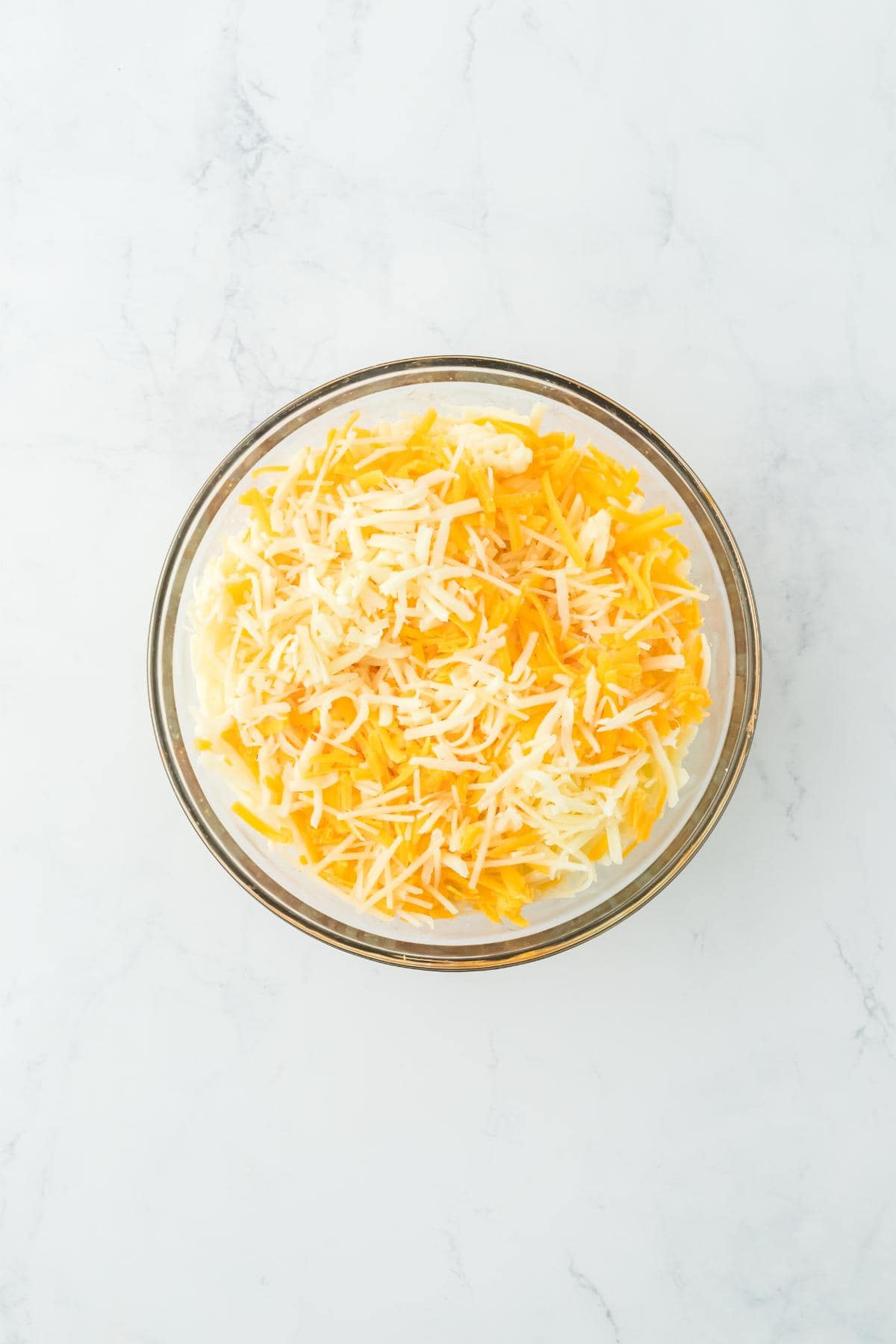 A bowl filled with shredded yellow and white cheeses, ready for mixing