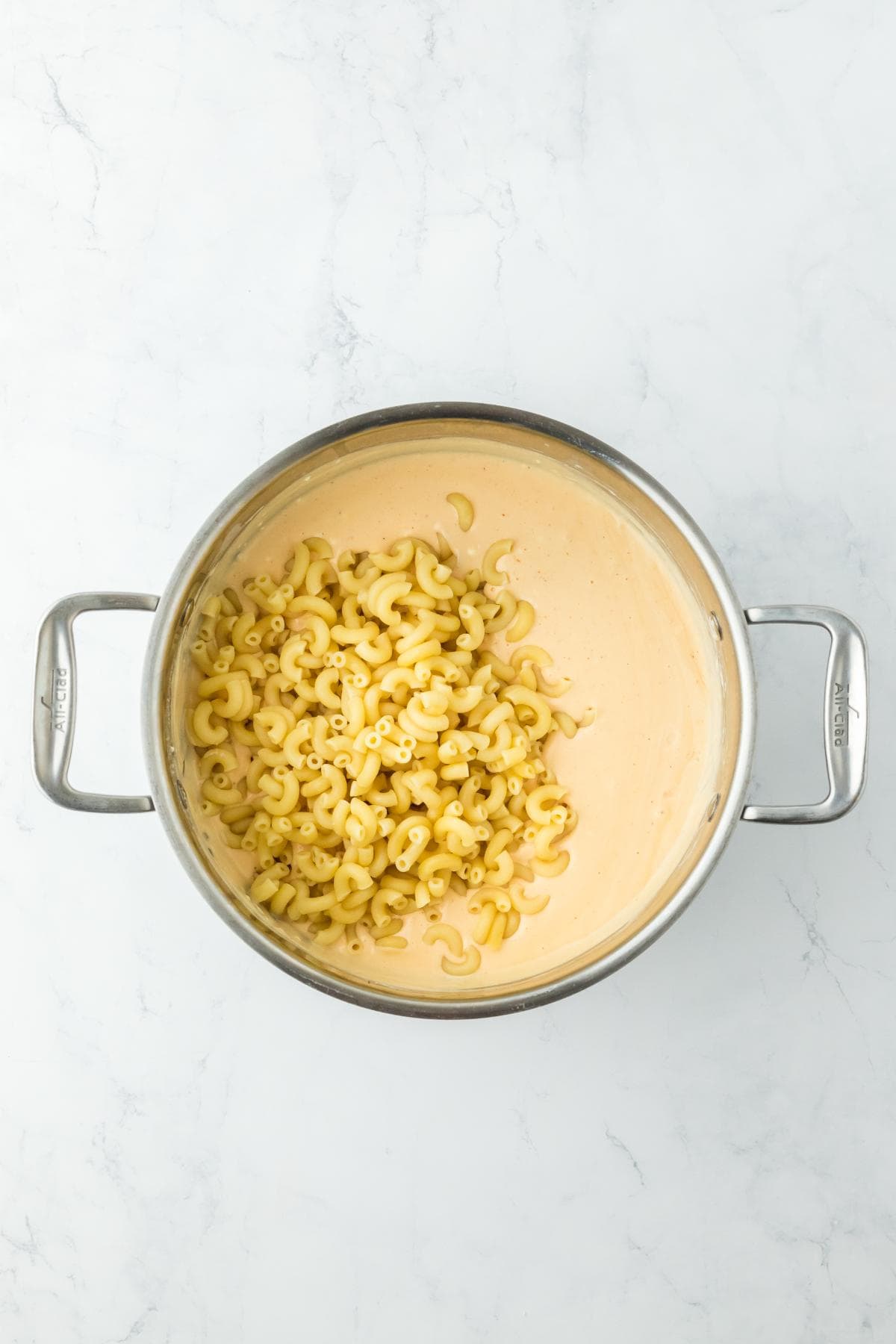 Cooked macaroni being stirred into the creamy cheese sauce in a large pot