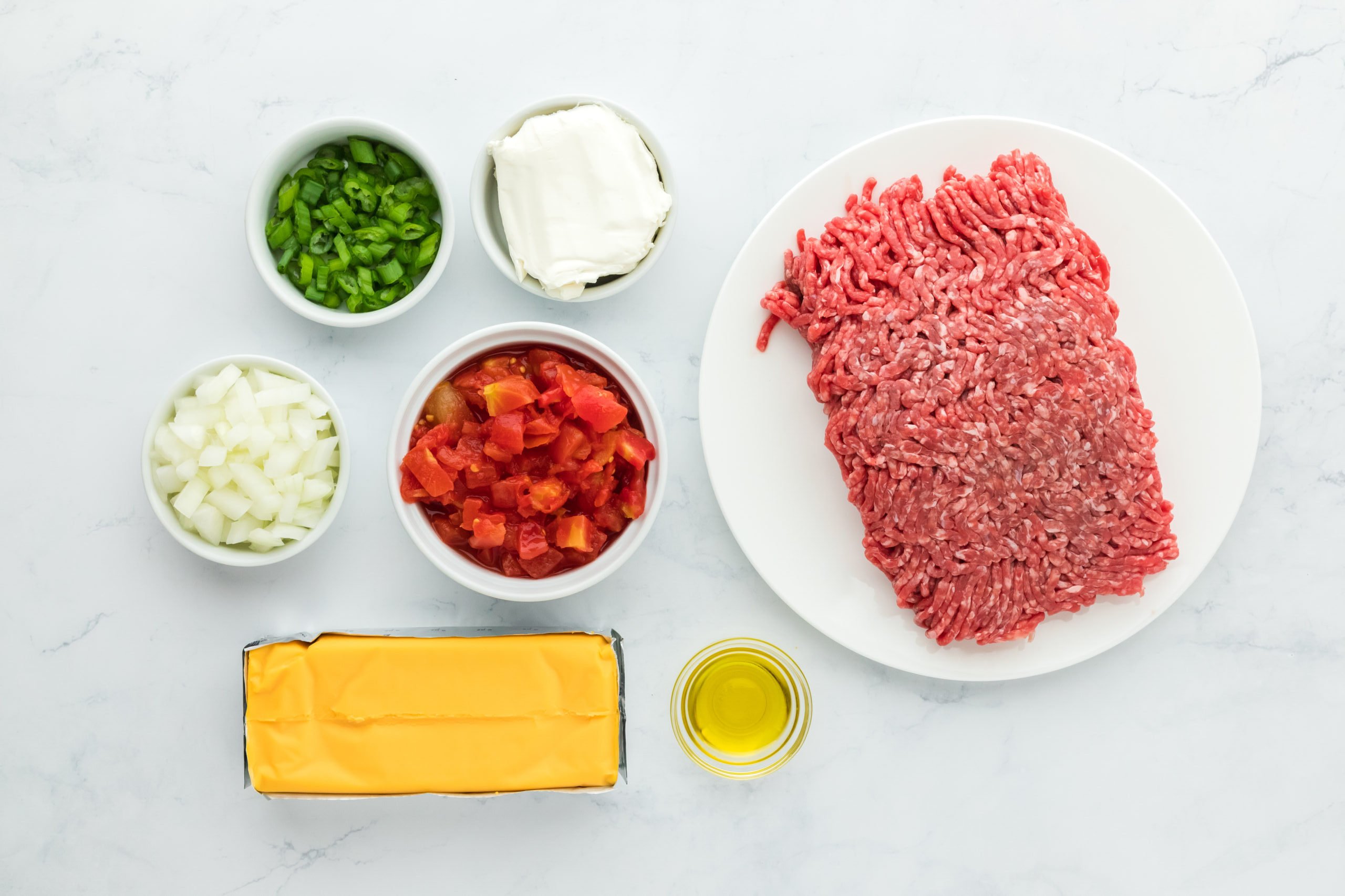 Ground beef, tomatoes, green onion, cheeses and onion on white countertop