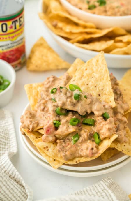 A white bowl of rotel dip with tortilla chips inside ready to serve on white background