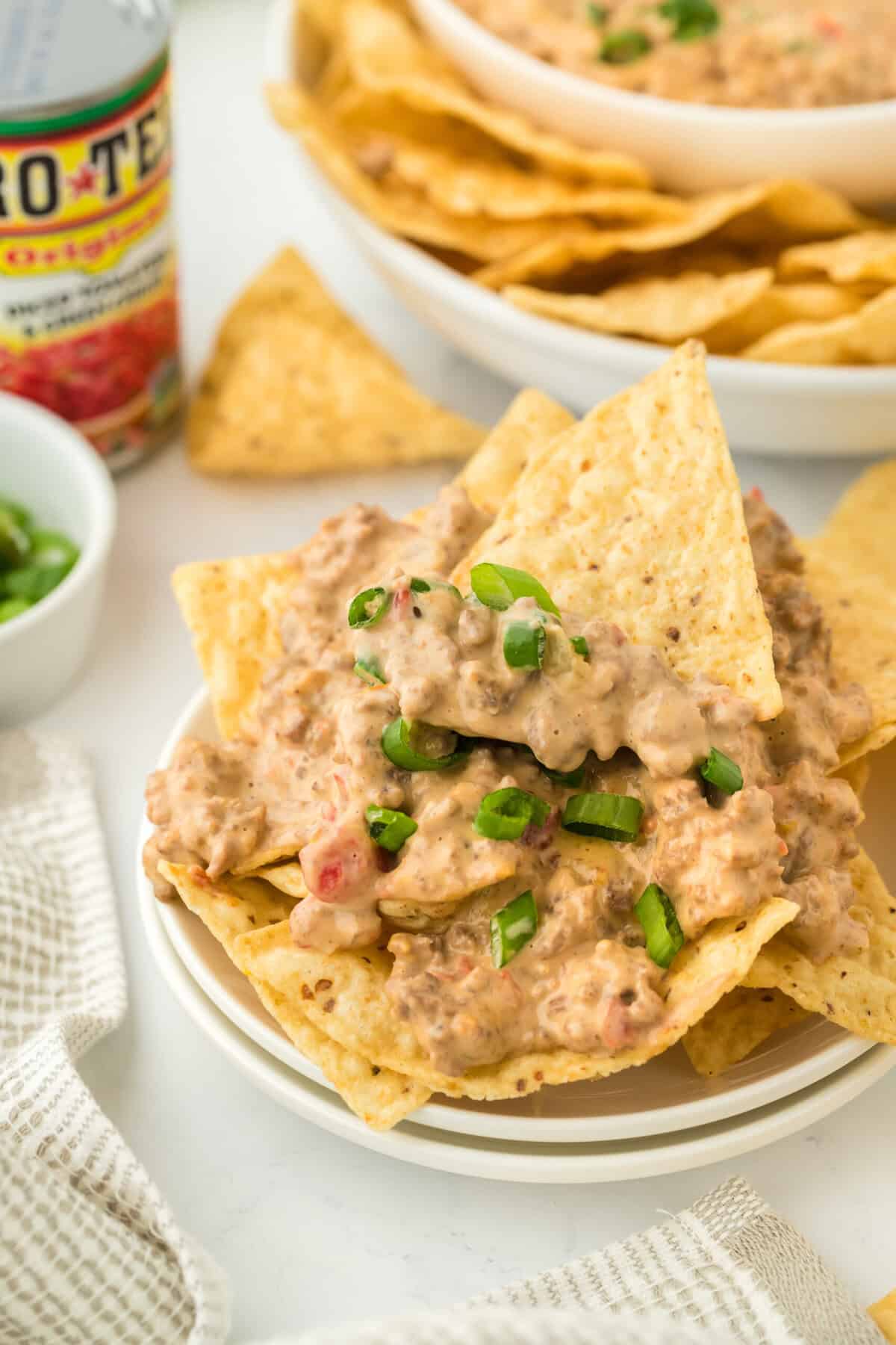 A white bowl of rotel dip with tortilla chips inside ready to serve on white background