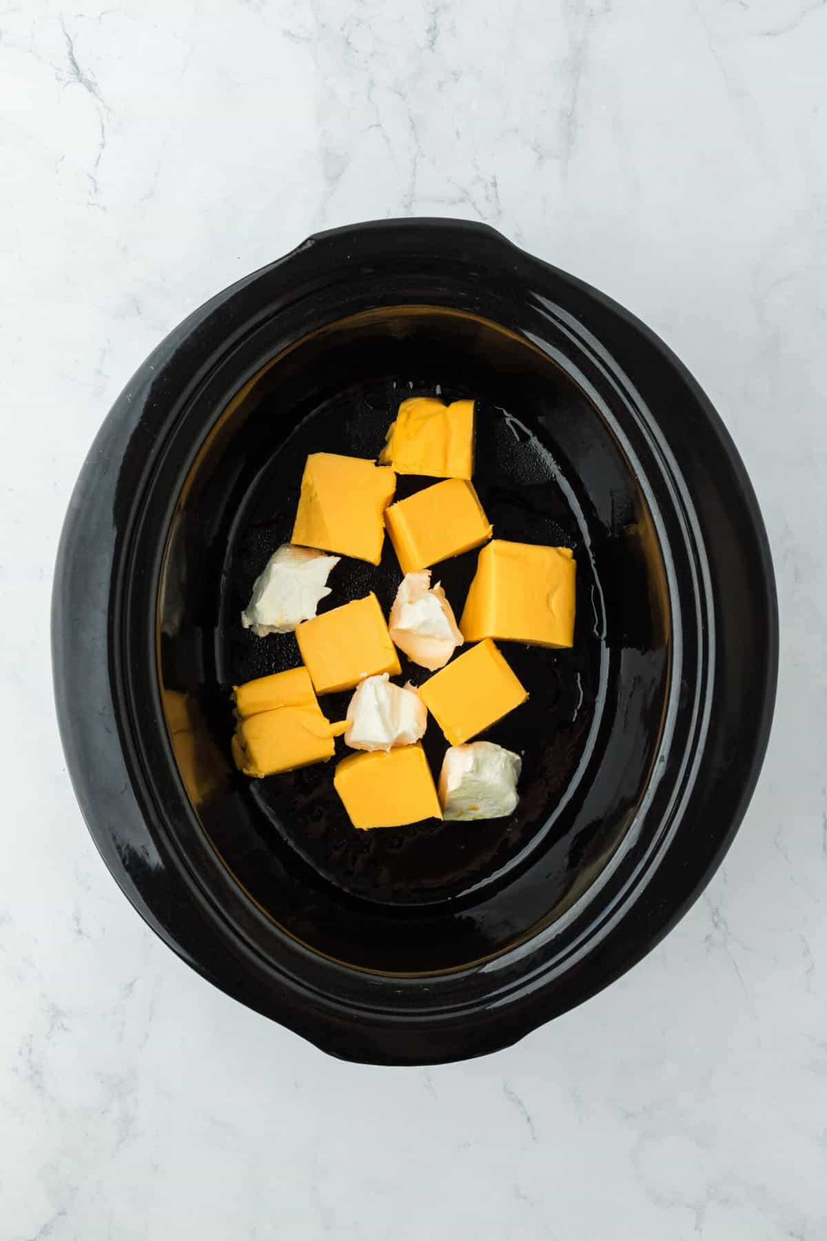 Two cheeses added to a slow cooker on a white countertop