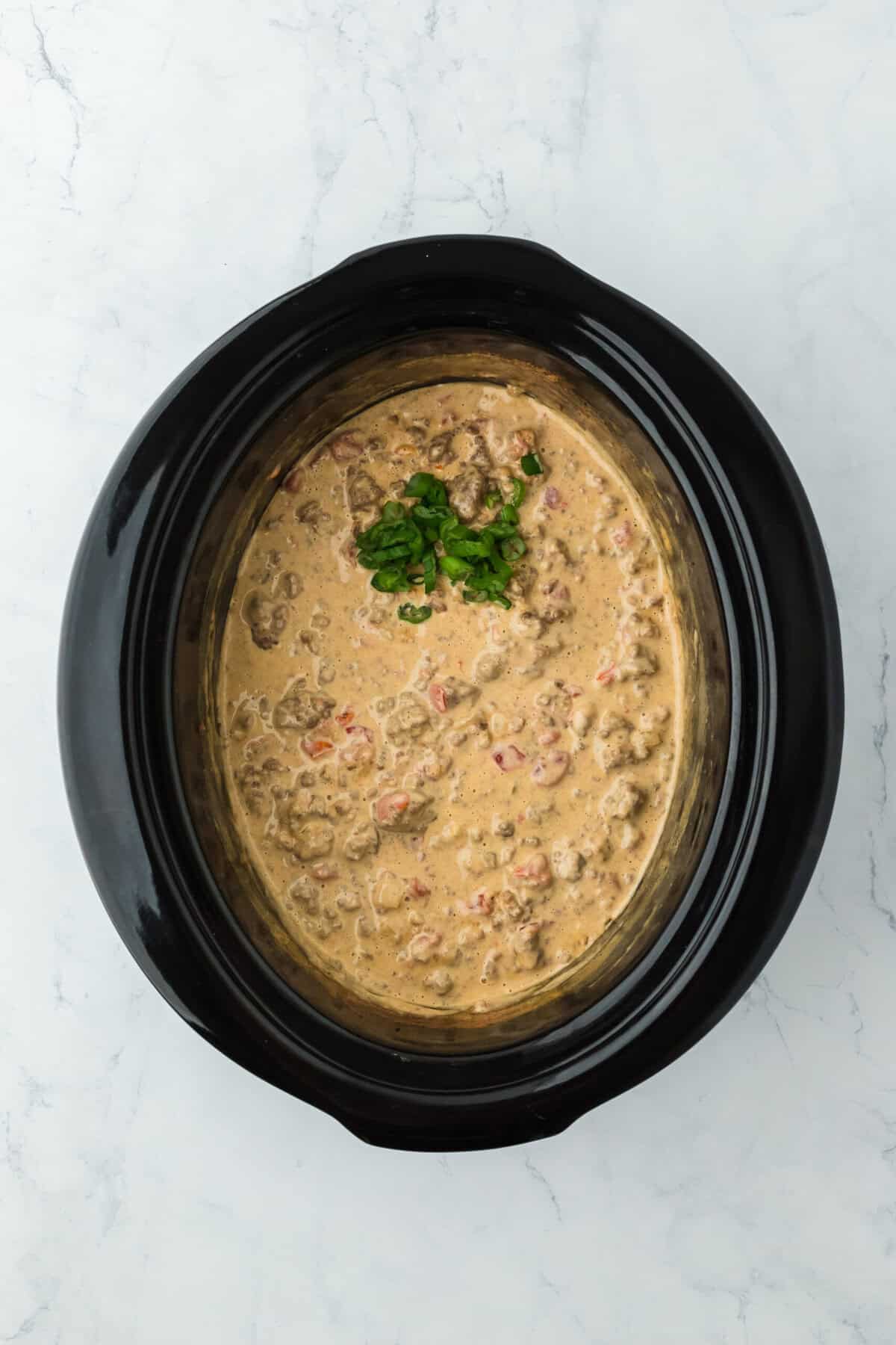 Completed rotel dip recipe in a slow cooker with green onion added