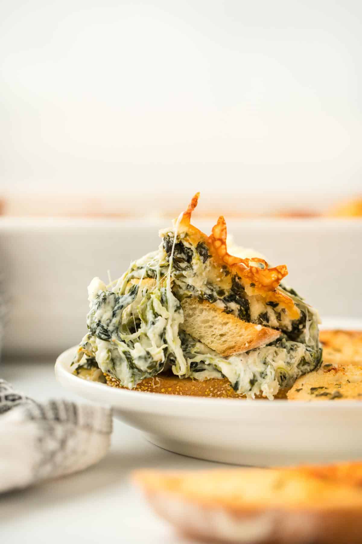 Plate with a portion of spinach dip topped with a crispy cheese piece, served with toasted bread