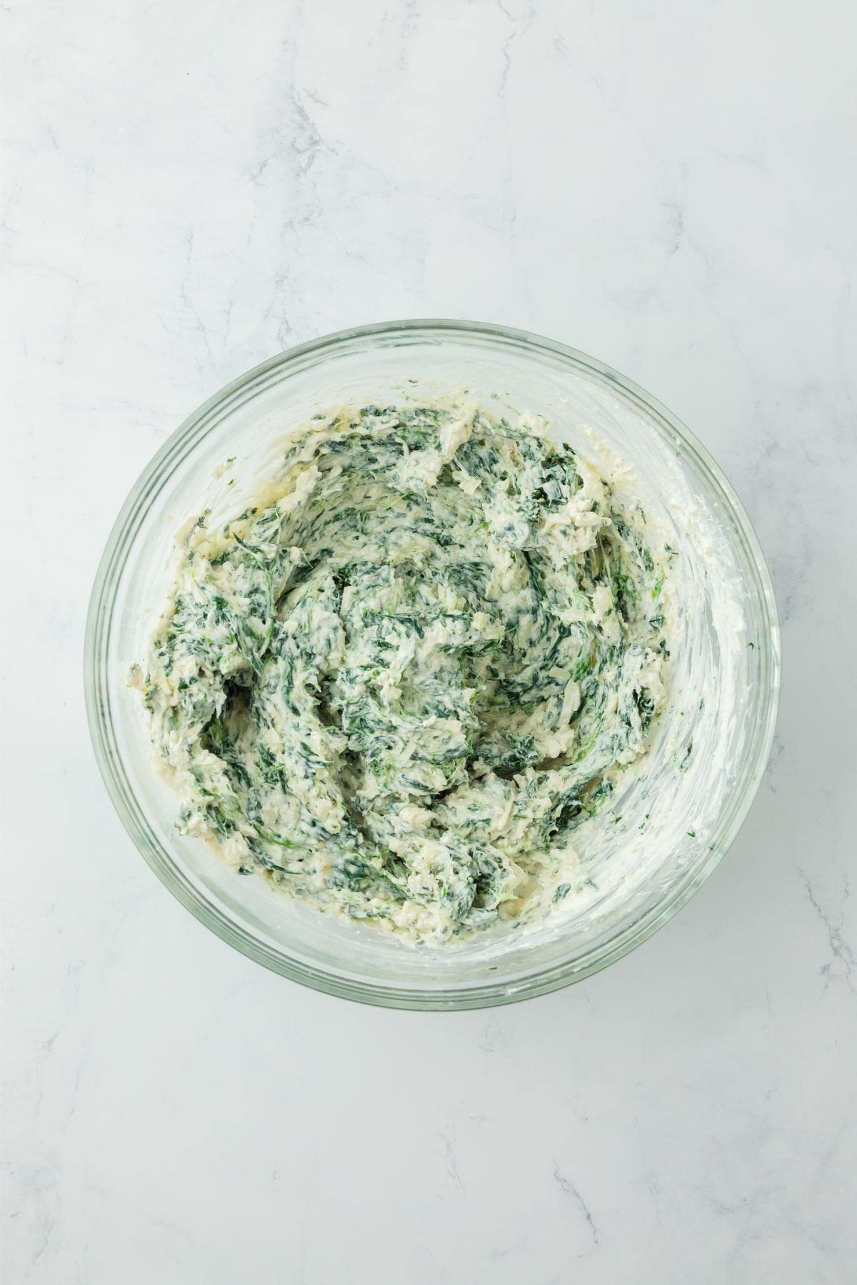 Fully mixed spinach dip in a glass bowl, ready for baking