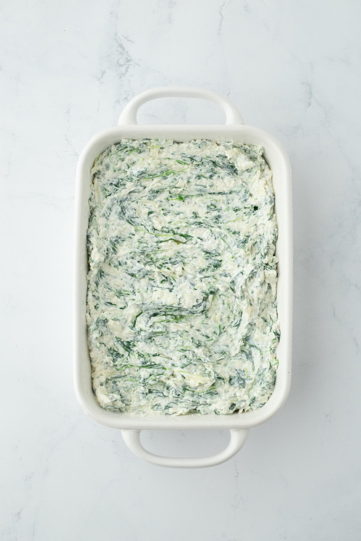 Unbaked spinach dip spread in a white casserole dish