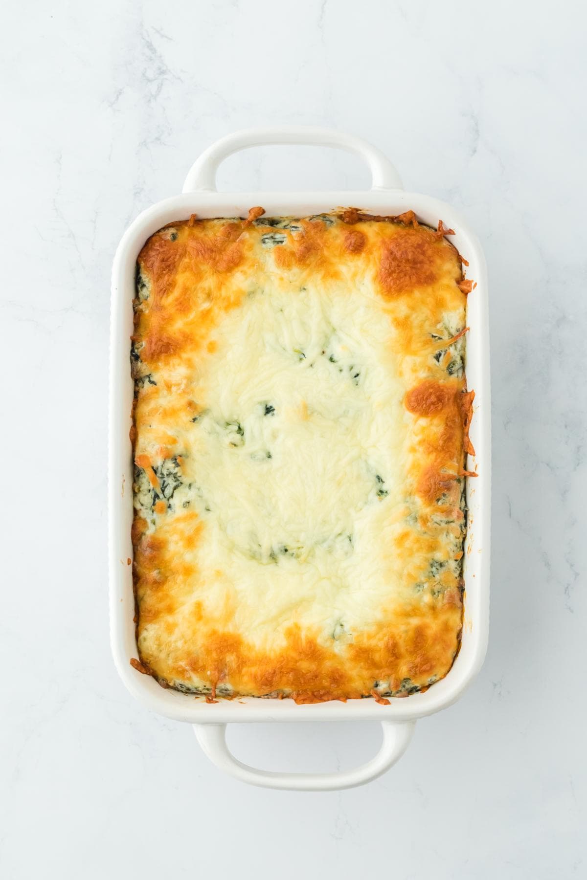 Fully baked spinach dip in a casserole dish with golden, bubbly cheese topping