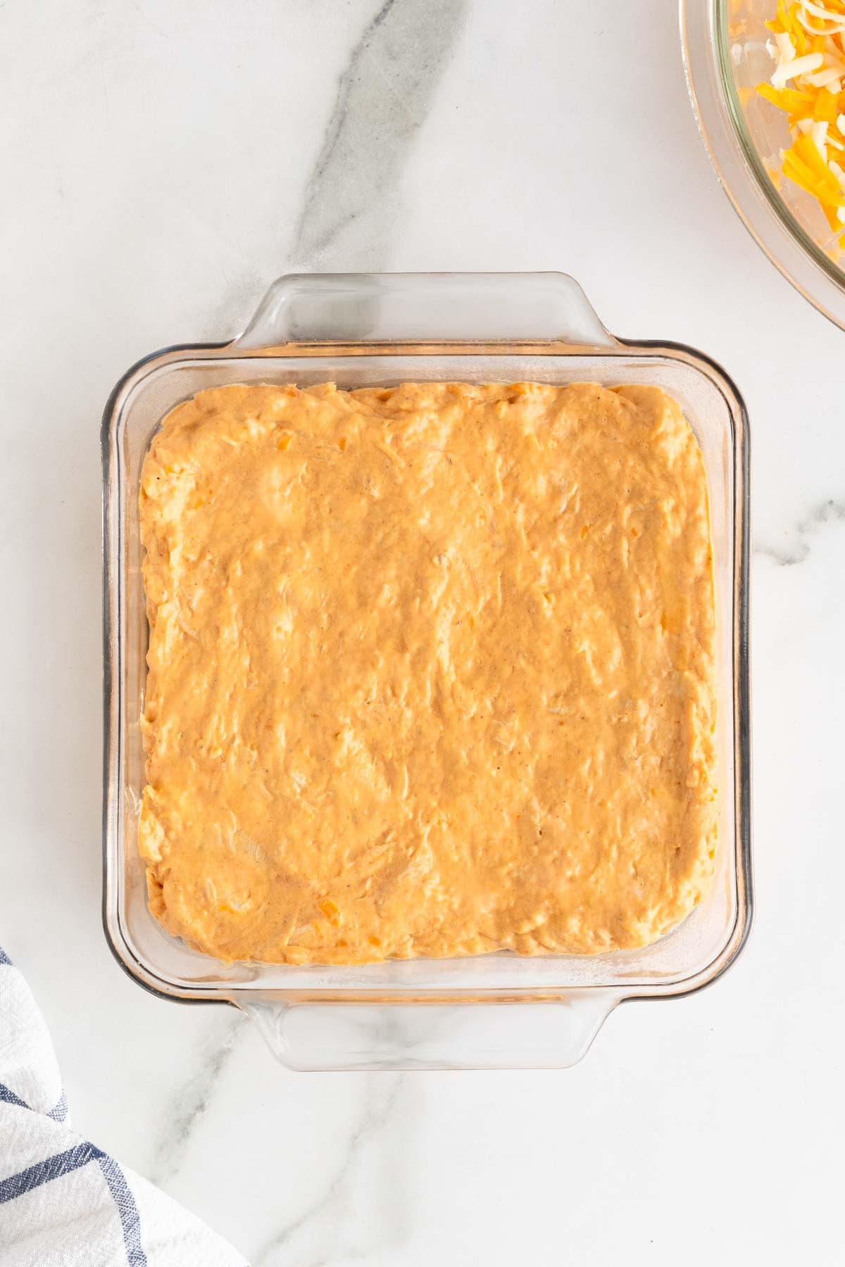 chicken dip added to a casserole dish before baking on a white countertop