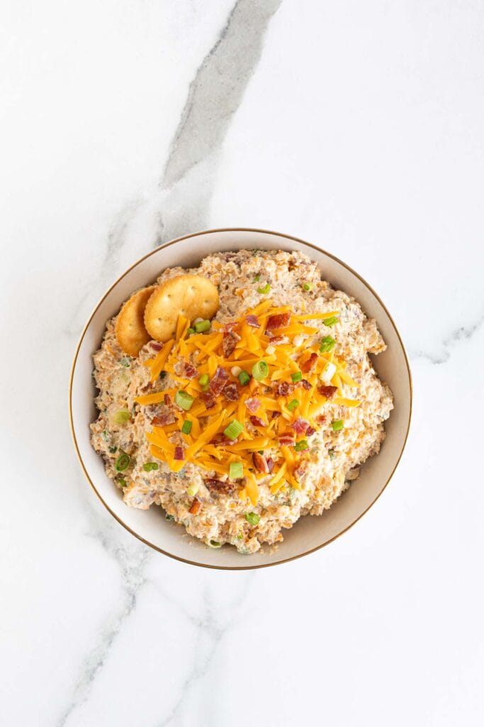 A bowl of the finished dip topped with cheddar cheese, bacon bits, and green onions, viewed from above