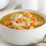 Closeup of a bowl of chicken and rolled dumplings soup with carrots and celery, garnished with fresh herbs