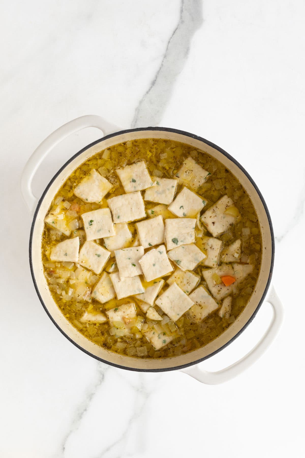 A pot of chicken and rolled dumplings with the dumplings floating on top of the soup