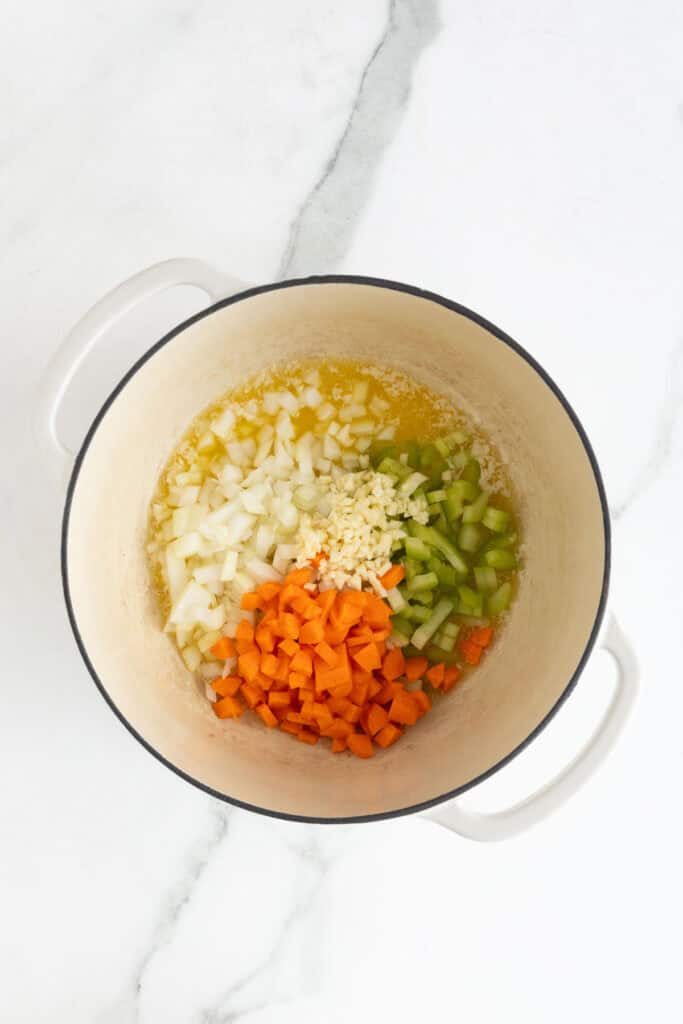 Chopped onions, carrots, celery, and garlic being sautéed in butter inside a pot