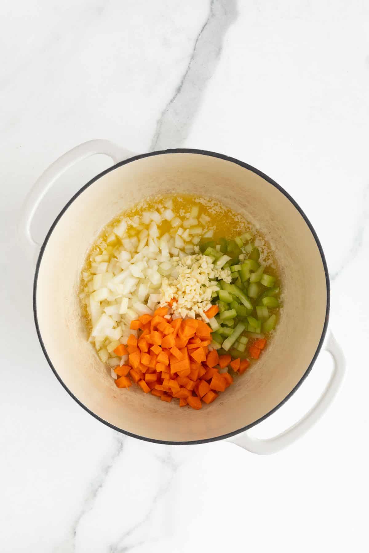 Chopped onions, carrots, celery, and garlic being sautéed in butter inside a pot