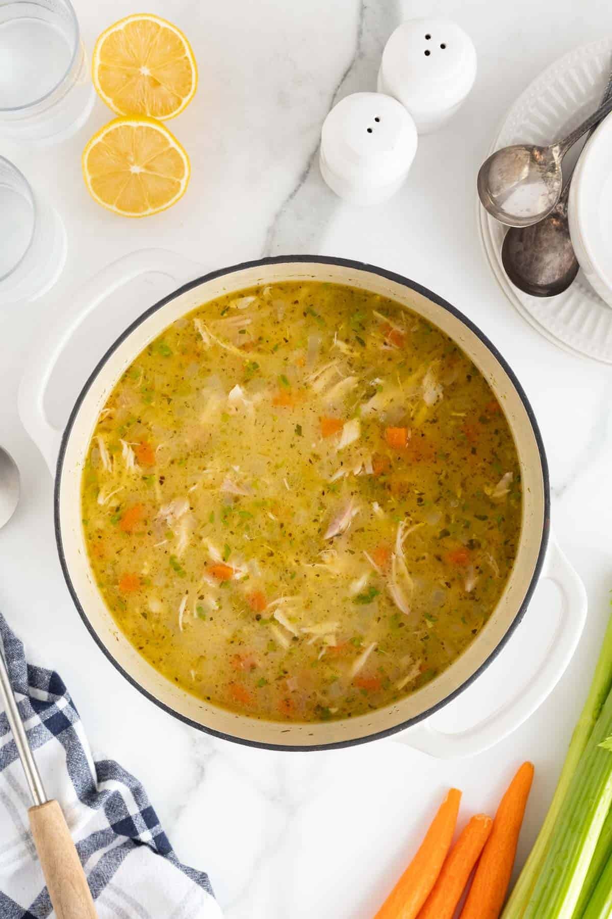 A wide shot of the completed chicken and rolled dumplings in the pot, with a fresh lemon, salt, pepper shakers, and vegetables surrounding the pot on the table