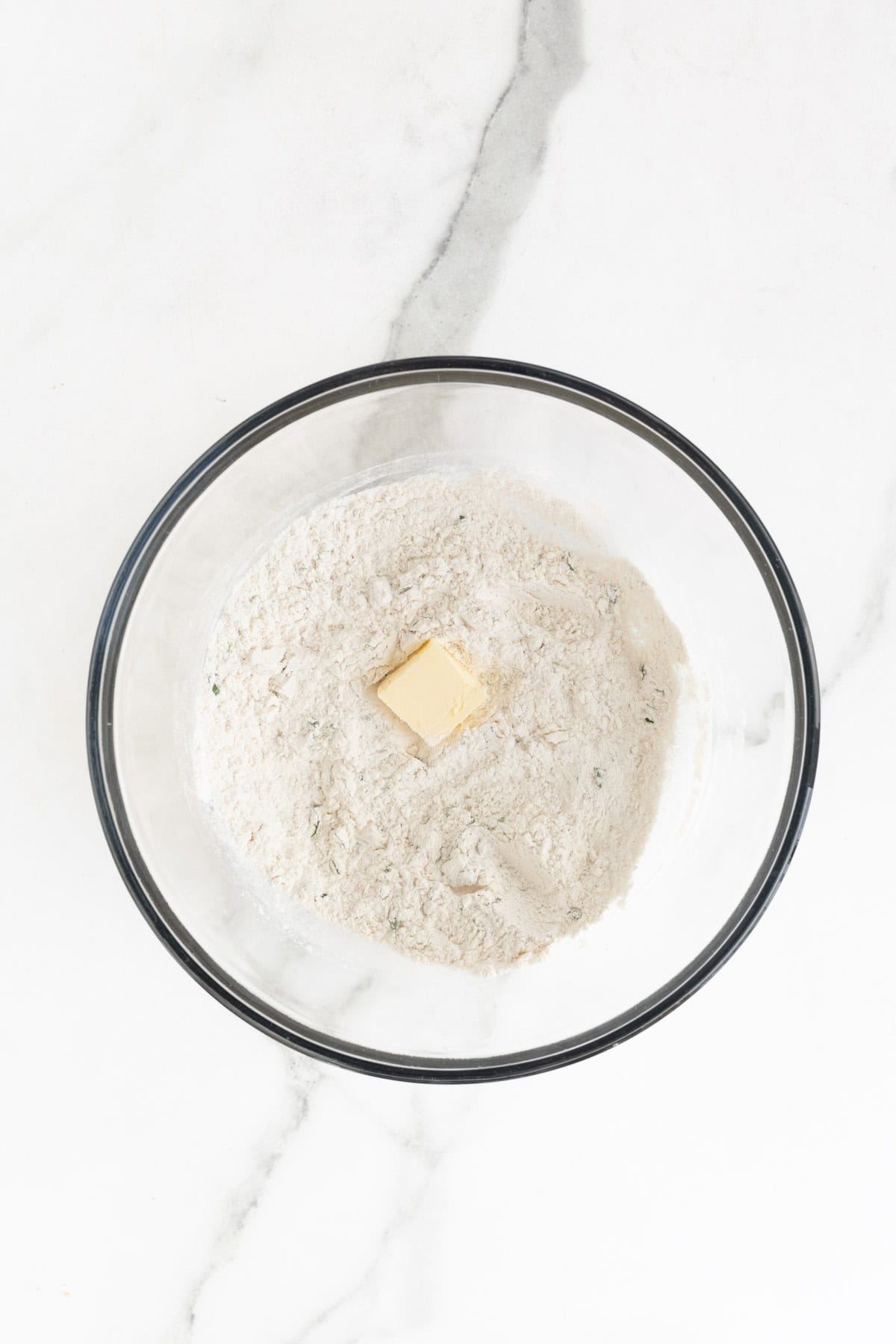 A chunk of butter added to the flour and herb mixture in a bowl