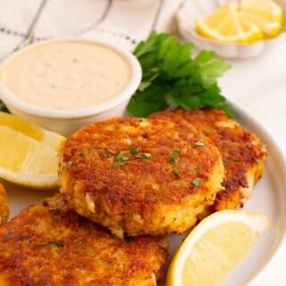 Perfect crab cakes on white plate with tartar sauce and lemon wedges