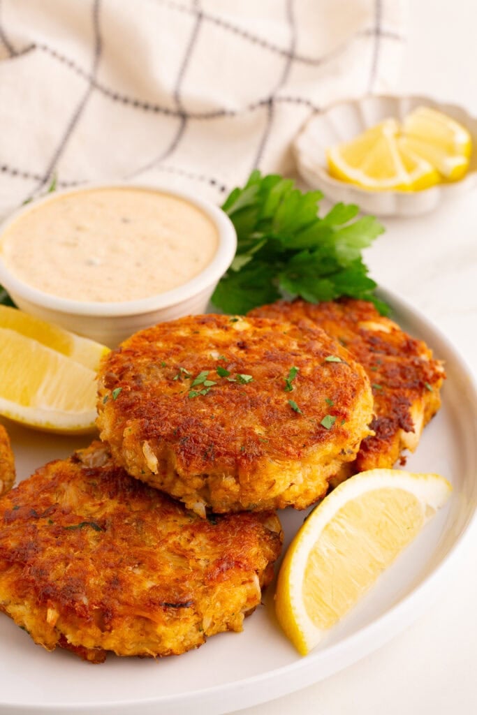 Perfect crab cakes on white plate with tartar sauce and lemon wedges