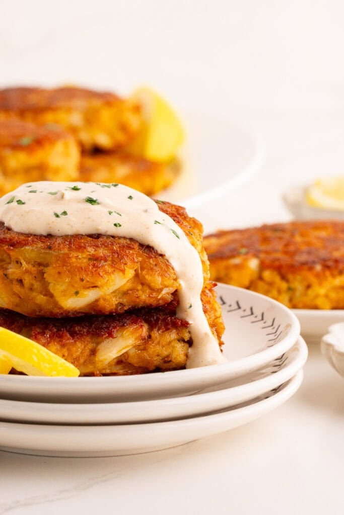 A close up of crab cakes ready to serve on white plates.