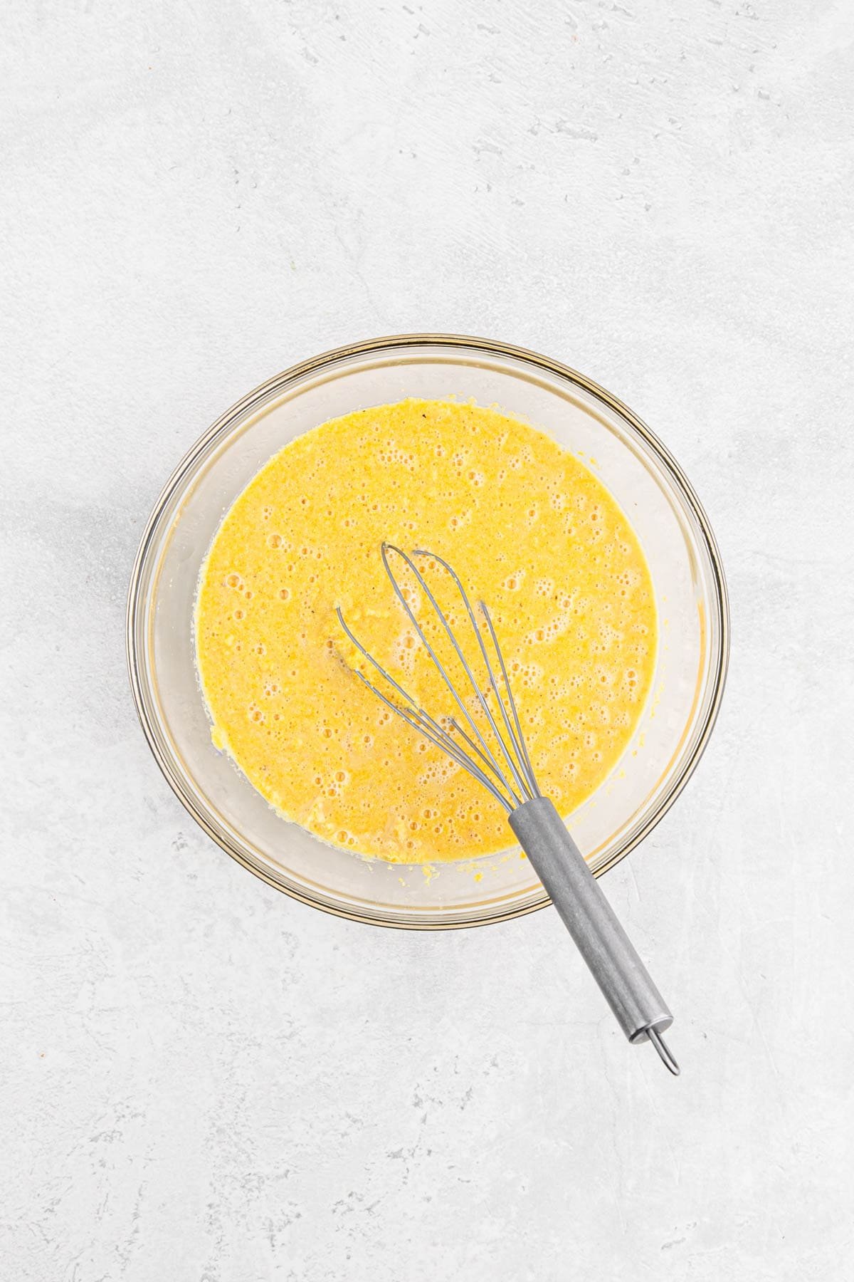 Cornmeal batter being mixed with a whisk in a glass bowl