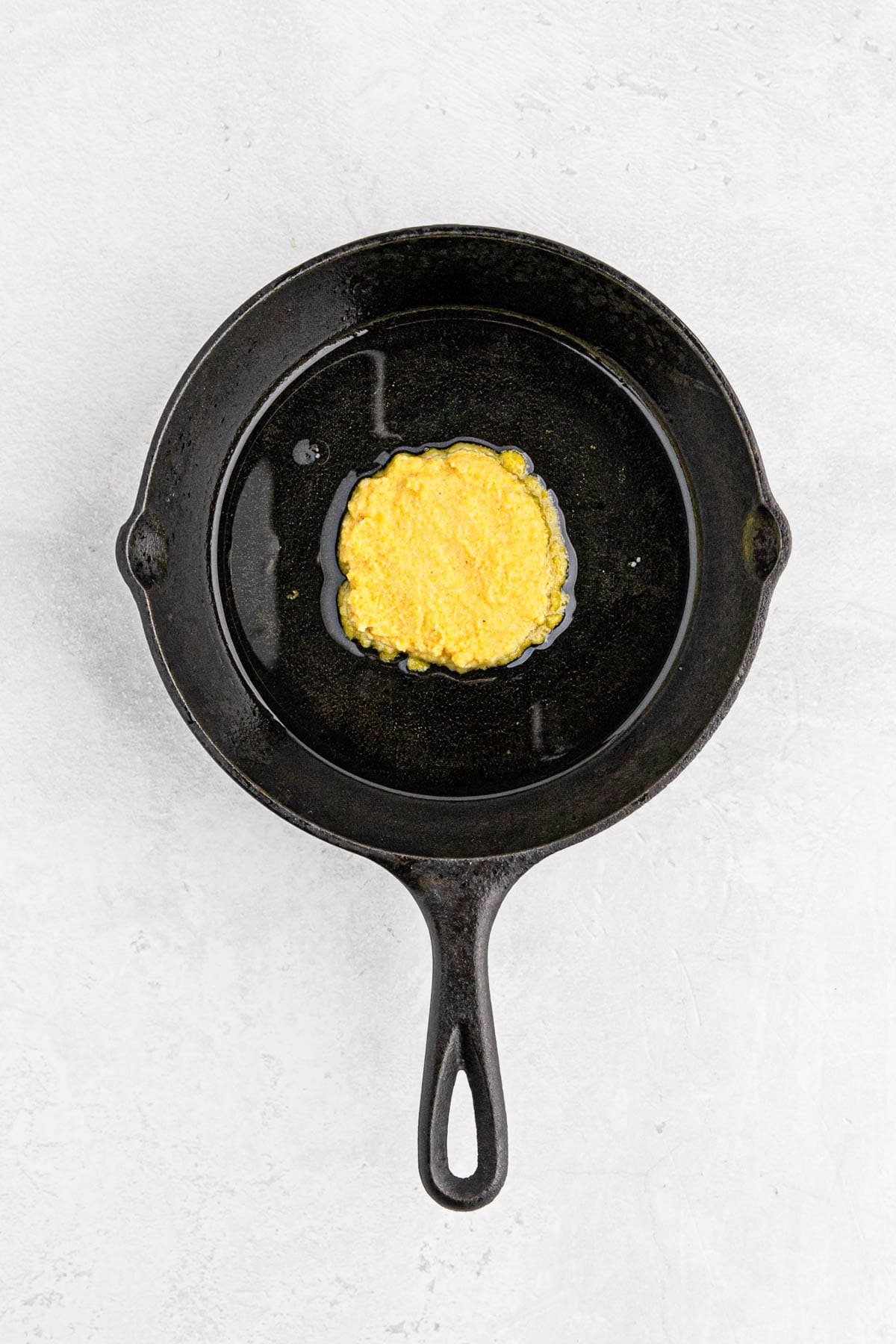 Hot water cornbread patty being fried in a cast iron skillet