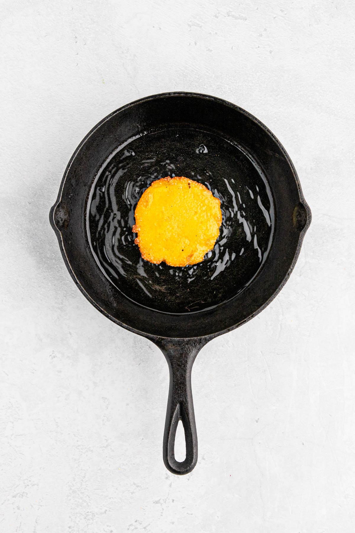 Hot water cornbread fritter frying in cast iron skillet