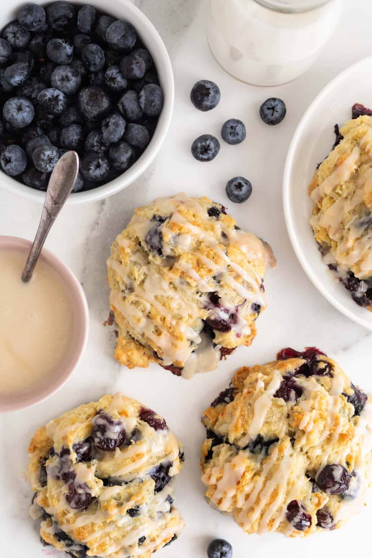 Blueberry biscuits on a white countertop with blueberries in a white bowl