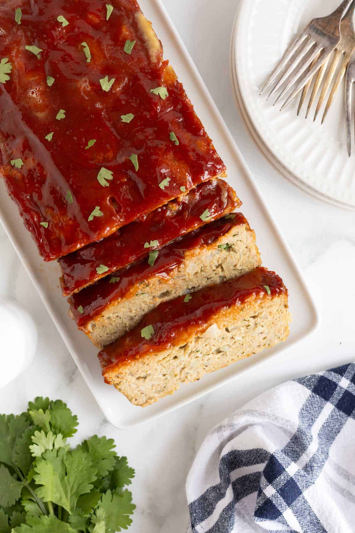 Overhead shot of turkey meatloaf slices on a platter with forks and plates beside it