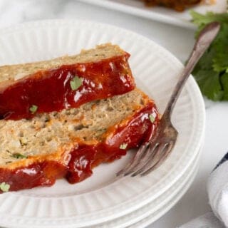 Closeup side view of two slices of glazed turkey meatloaf stacked on a plate with a fork