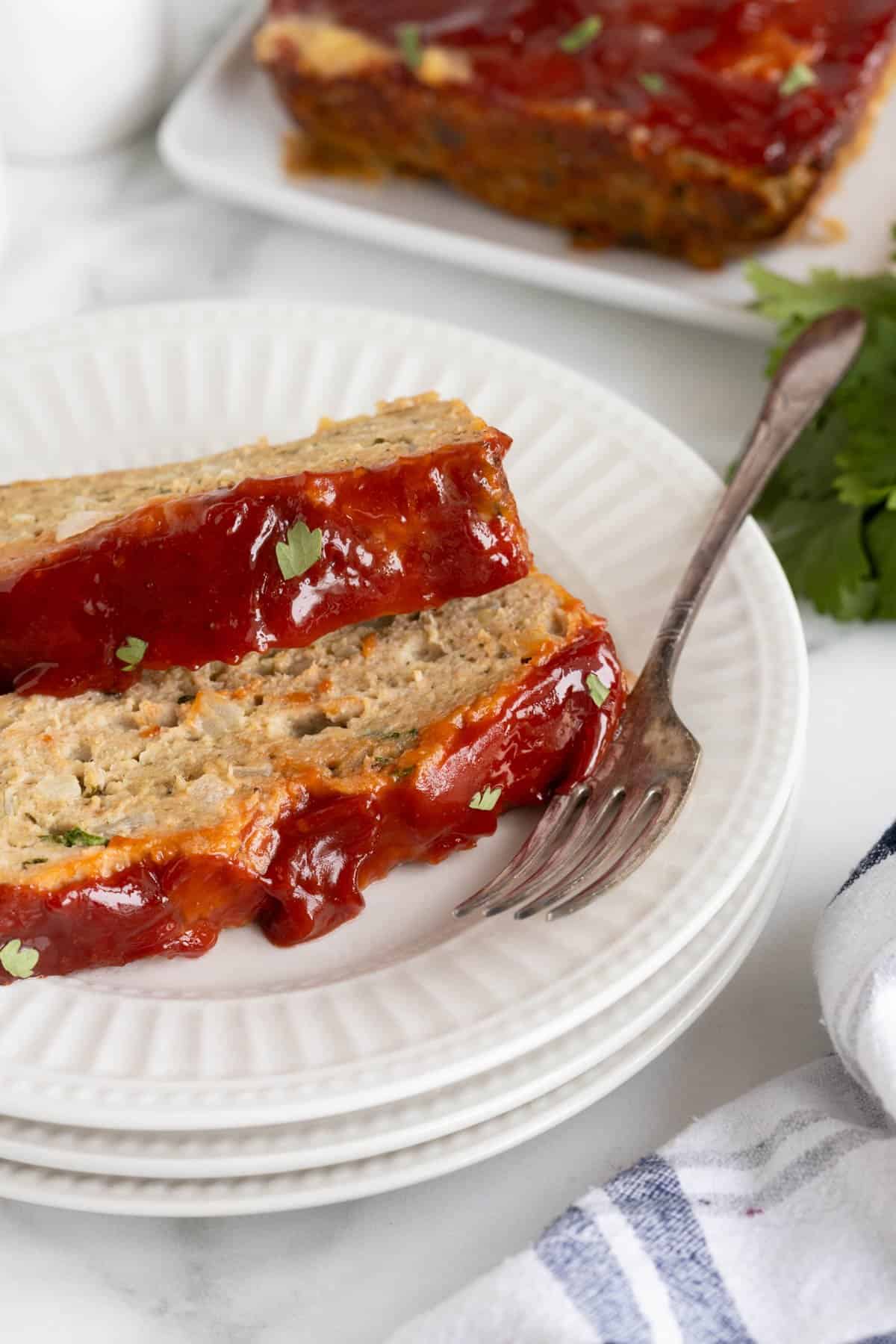 Closeup side view of two slices of glazed turkey meatloaf stacked on a plate with a fork