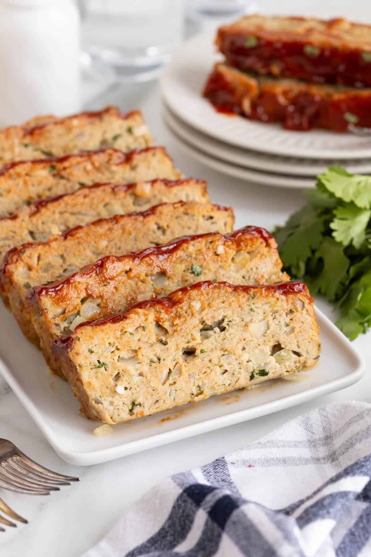 Closeup of several turkey meatloaf slices arranged on a serving plate with more slices in the backgound