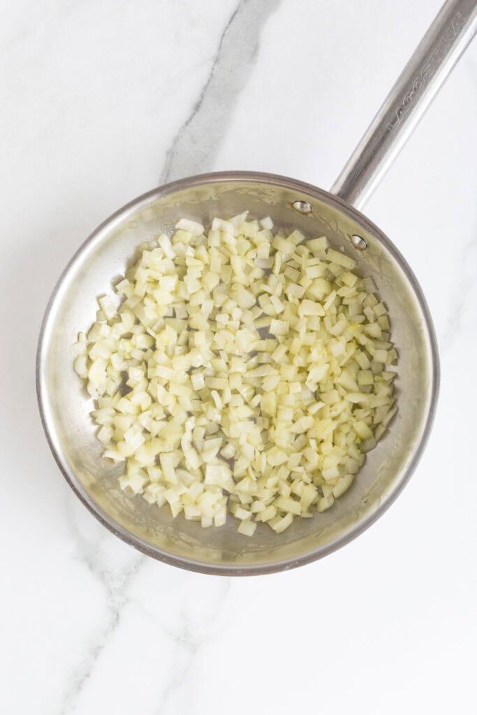 Diced onions being sautéed in a stainless steel skillet