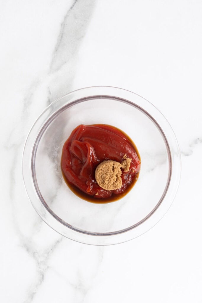 A clear bowl with ketchup, brown sugar, and Worcestershire sauce ready to be mixed for the glaze