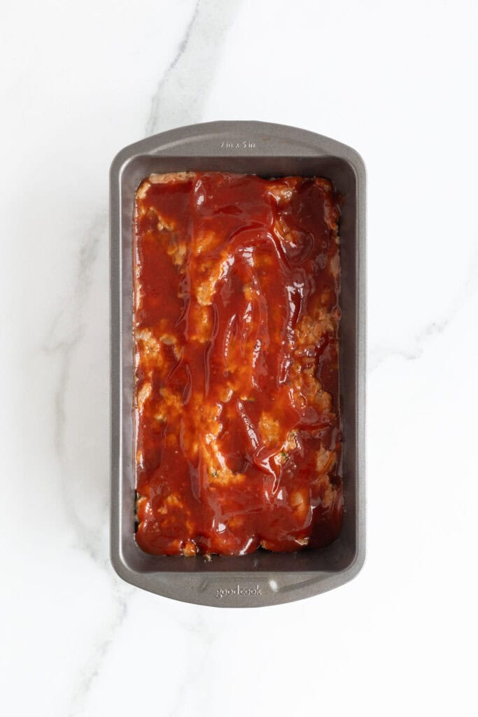 Raw turkey meatloaf in a loaf pan topped with the prepared ketchup glaze