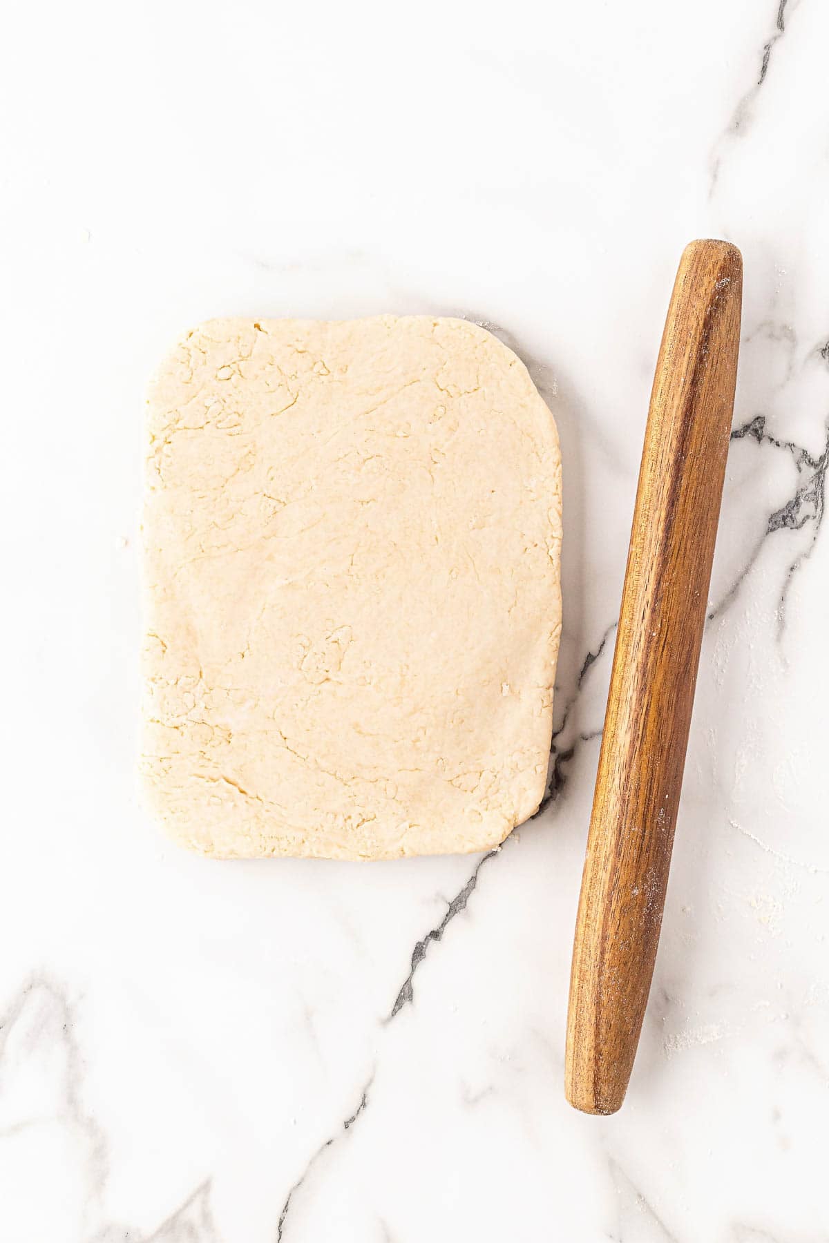 Buttermilk biscuit dough pressed into rectangle beside rolling pin