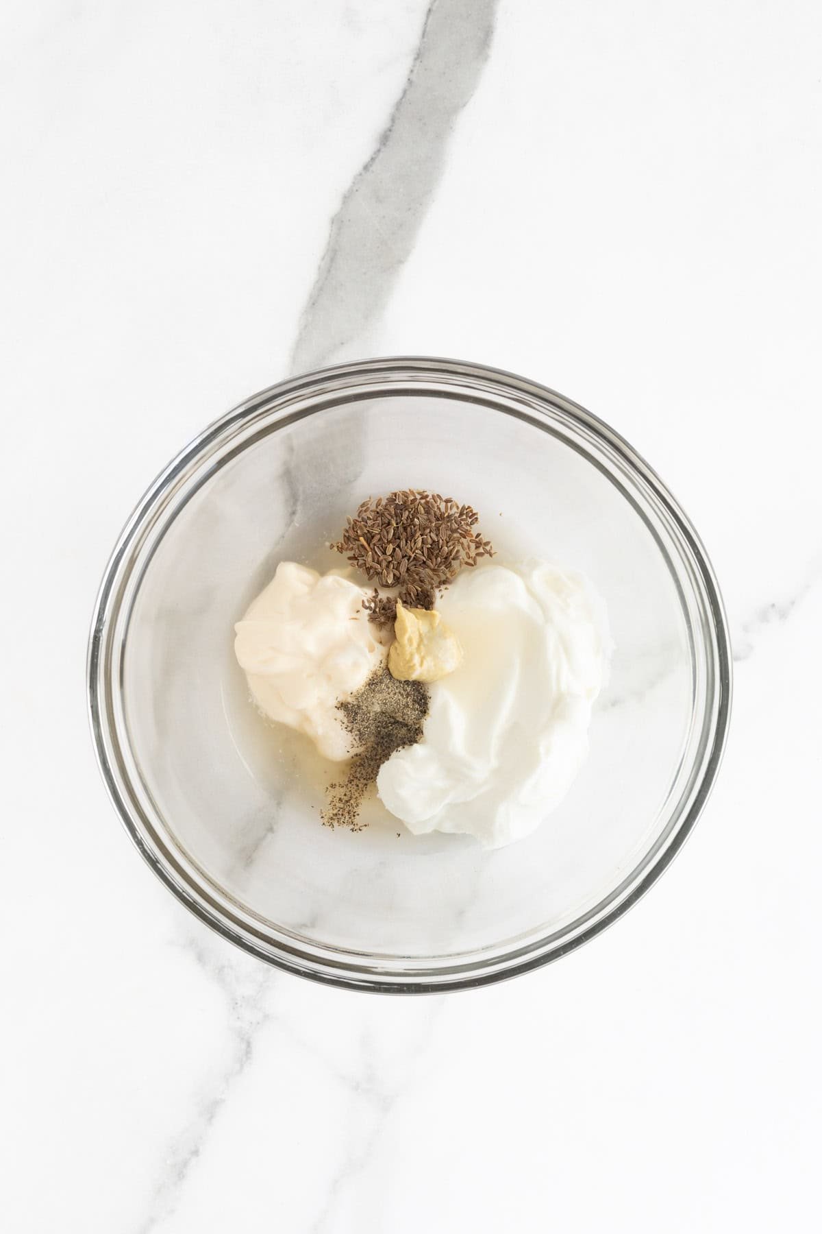 A glass bowl containing coleslaw dressing ingredients