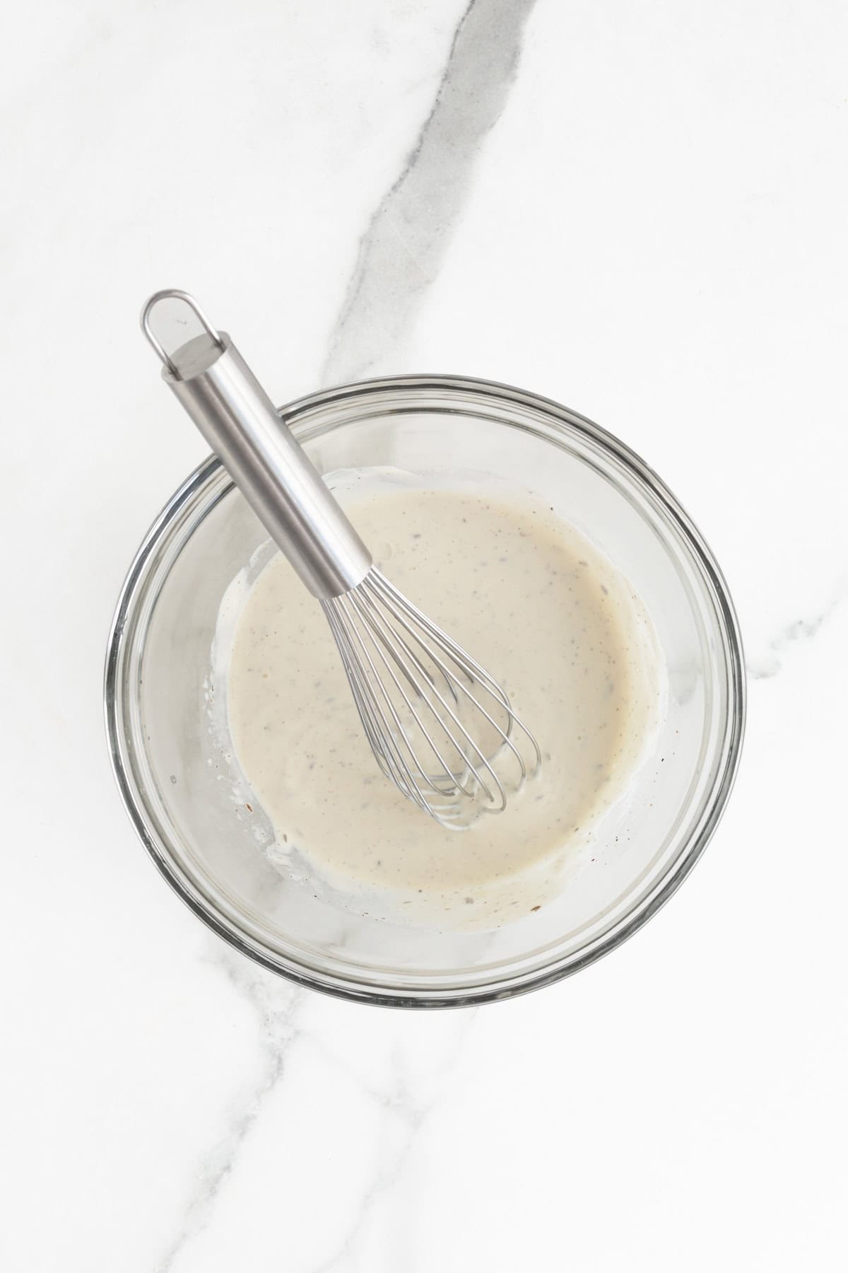 A glass bowl with coleslaw dressing being whisked to a smooth consistency