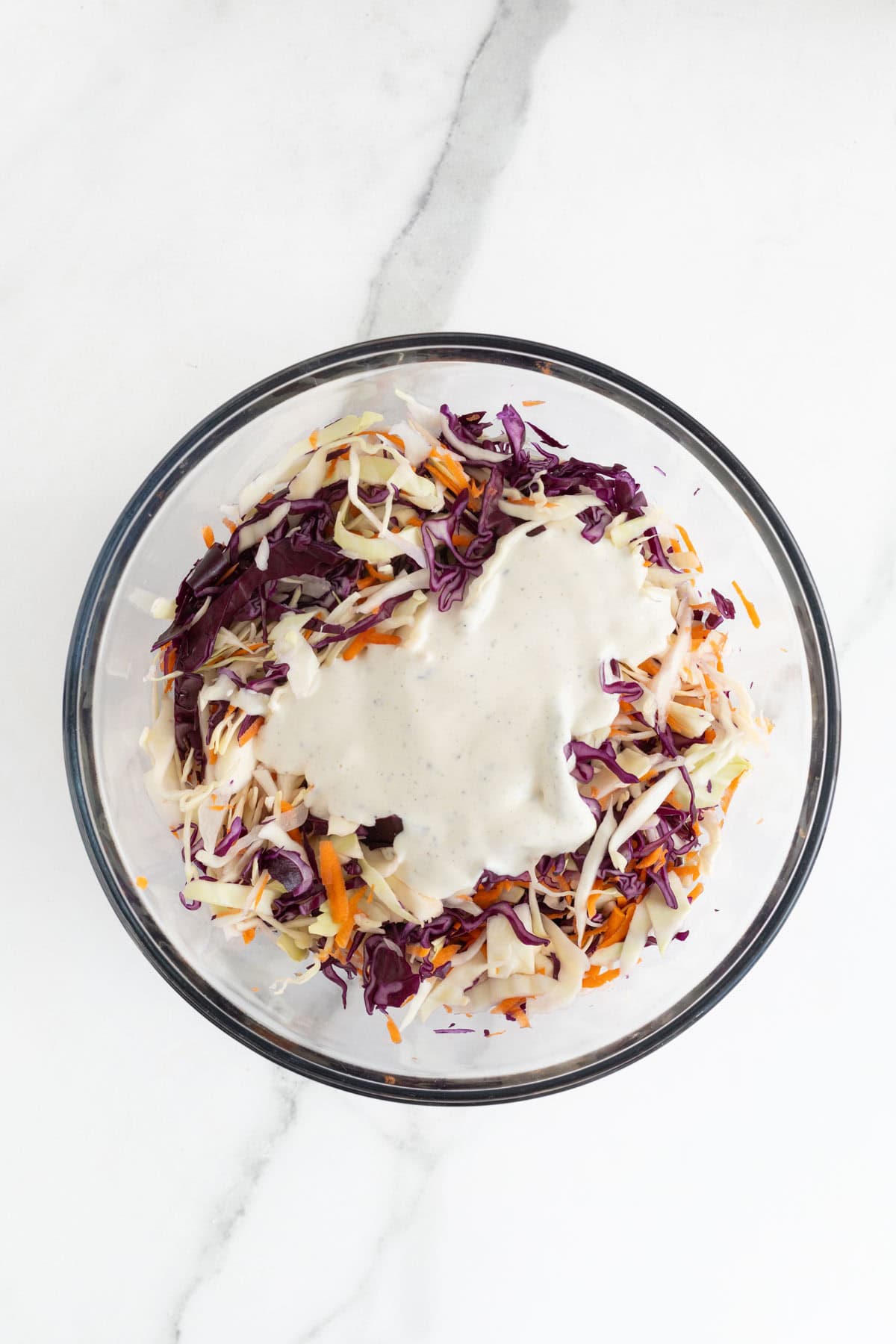 A glass bowl with mixed cabbage and carrots, with coleslaw dressing poured on top