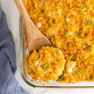 A wooden spoon scooping out a portion of funeral potatoes out of a glass baking dish