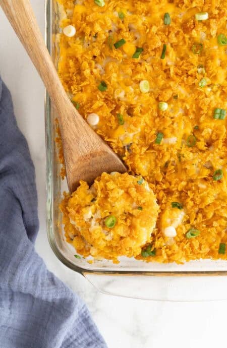 A wooden spoon scooping out a portion of funeral potatoes out of a glass baking dish