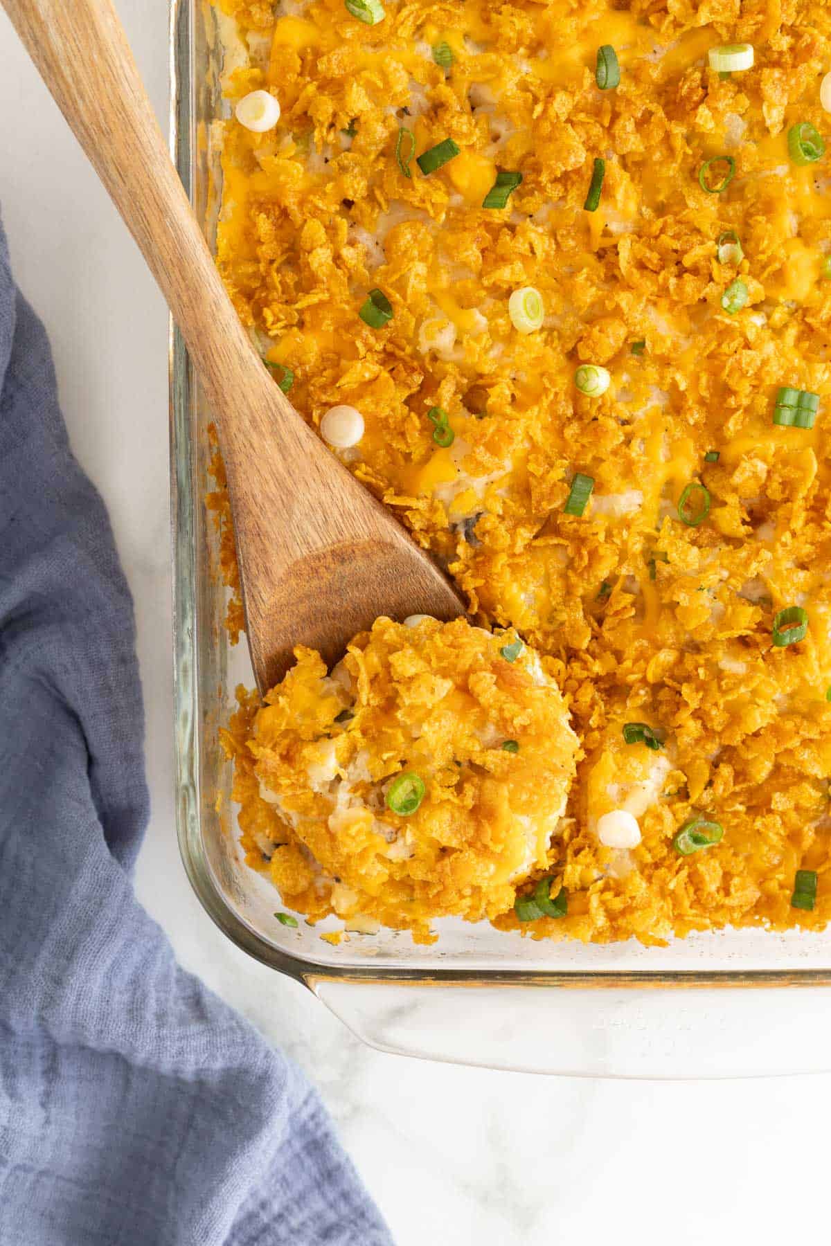 A wooden spoon scooping out a portion of funeral potatoes out of a glass baking dish