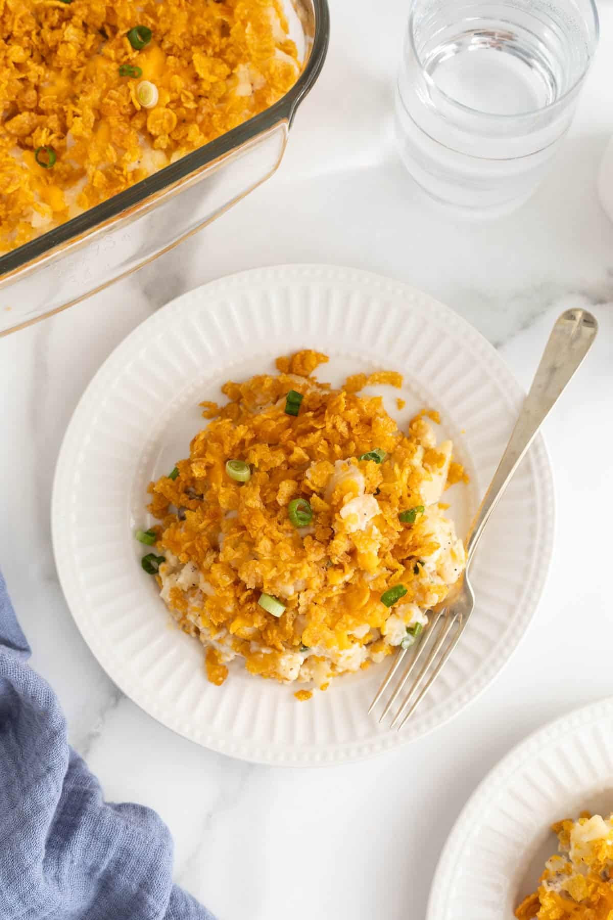 A plateful of funeral potatoes next to a glass baking dish with more casserole