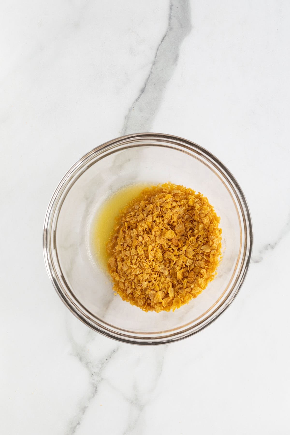 A small glass bowl with crushed cornflakes partially mixed with melted butter