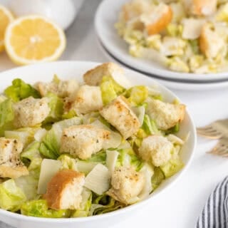 Caesar salad on a bowl, with another bowl of salad in the background next to fresh lemon and dressing